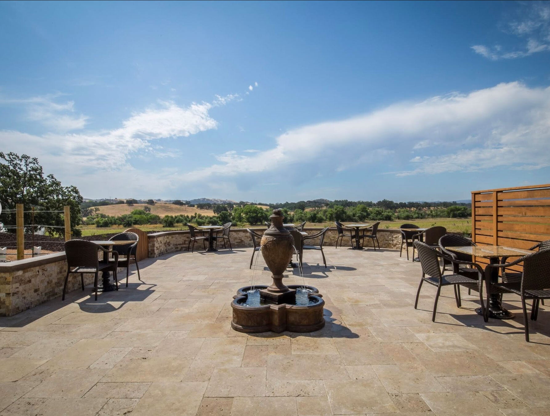 Outdoor patio area with tables, chairs, and a fountain under a clear blue sky.